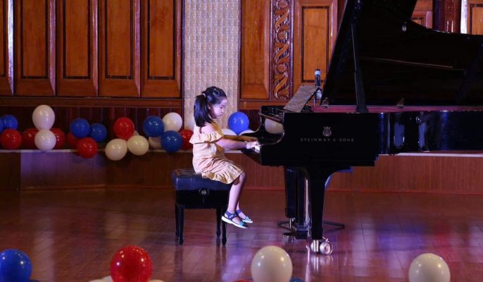 Học sinh nhỏ tuổi biểu diễn piano trên sân khấu với đàn grand piano chuyên nghiệp